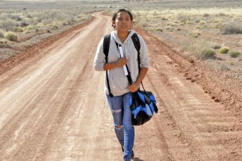 Young woman walking with a shoulder bag on a dirt road in the desert